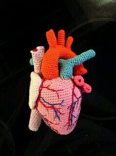 a crocheted human heart hanging on a black surface with other items around it