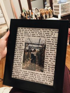 a person holding up a framed photo in front of a table with pictures on it