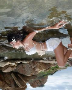 a woman in white swimsuit floating on rocks next to water