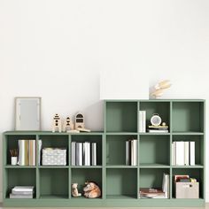 a green shelf with books and toys on it in front of a white painted wall