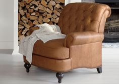 a brown leather chair sitting in front of a fire place with logs on the floor