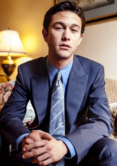 a man in a suit and tie sitting on a couch with his hands folded out