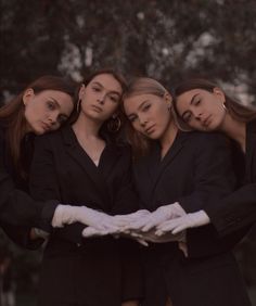 four women in black suits and white gloves posing for the camera with their arms wrapped around each other