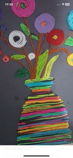 a vase filled with lots of different colored paper flowers on top of a gray surface