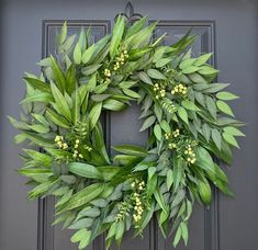 a wreath is hanging on the door with green leaves and yellow flowers in front of it