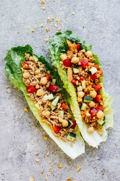 two lettuce wraps filled with meat, vegetables and nuts on a gray surface