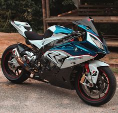 a silver and blue motorcycle parked on top of a parking lot next to a wooden structure