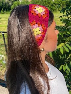 a woman wearing a pink crocheted headband with flowers on it and trees in the background