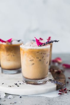 two glasses filled with ice cream on top of a white plate and garnished with pink flowers