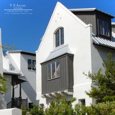 a white house with grey shutters and trees in the foreground on a sunny day