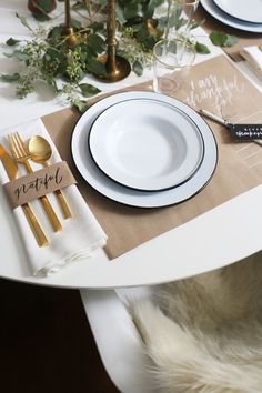 a table set with white and gold place settings, napkins, silverware and greenery