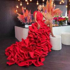 a woman in a red dress standing next to a table with flowers and feathers on it