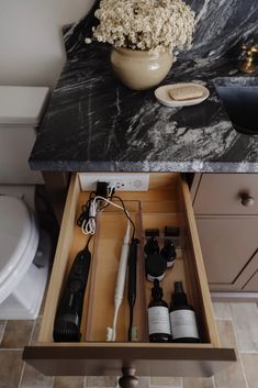 an open drawer in a bathroom with hairdryers and other items on the counter