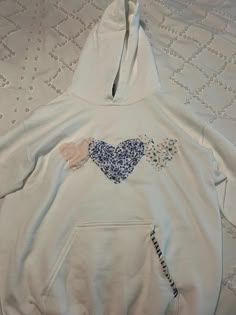 a white hoodie with blue and pink hearts on the front, sitting on a bed