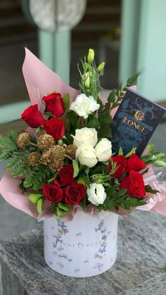 a bouquet of red and white flowers sitting on top of a stone table next to a book