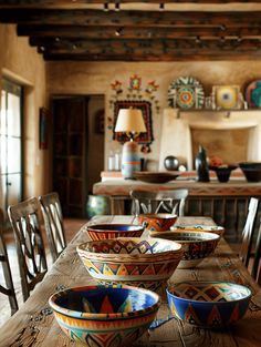 several bowls are sitting on a table in the middle of a room with wooden chairs