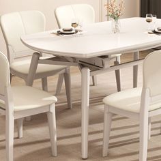 a white dining table with four chairs around it and a vase on the table next to it