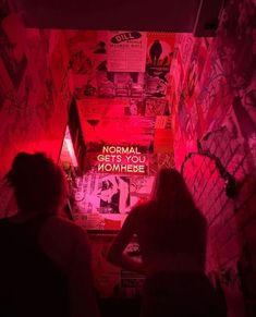 two people standing in front of a wall covered with posters and graffiti, looking up at the ceiling