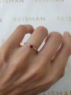 a woman's hand wearing a gold ring with a ruby stone on the band