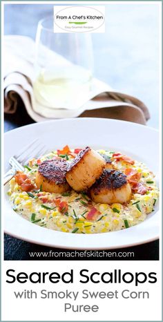 seared scallops with smoky sweet corn puree on a white plate next to a glass of wine