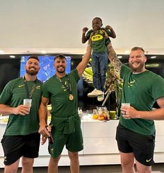 three men in green shirts holding up a statue