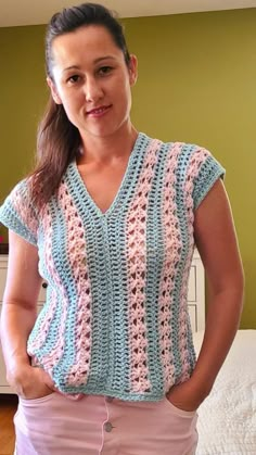 a woman standing in front of a bed wearing a crocheted shirt and pink pants