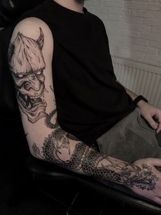 a man with a dragon tattoo on his arm sitting in a chair next to a brick wall