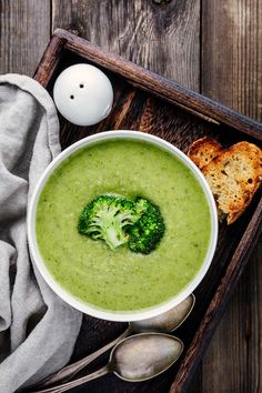 a bowl of broccoli soup on a tray next to bread and spoons