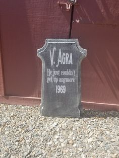 a tombstone sitting on the side of a building next to a red door that says v agra he just couldn't get up anymore