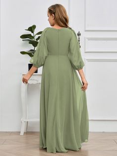 a woman in a green dress standing next to a white table and potted plant