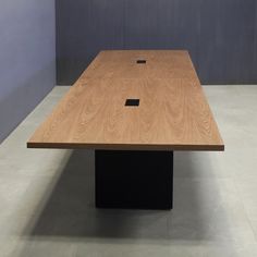 a wooden table with black square bases in an empty room on concrete flooring and walls