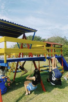 three children playing on a colorful playground set in the grass with their arms and legs up