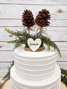 a white cake with pine cones on top and the word forever written in black lettering