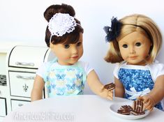 two dolls are sitting at a table eating cookies