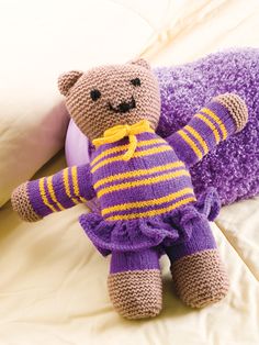 a teddy bear laying on top of a bed next to a purple pillow and blanket