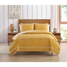 a bed with yellow bedspread and pillows in a room next to a window