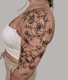 a woman's shoulder with flowers and leaves on her arm, which is covered in black ink