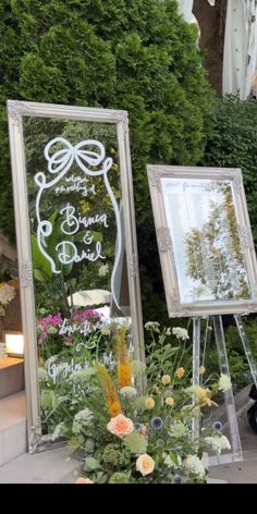 a couple of mirrors sitting next to each other on top of a sidewalk with flowers in front of them