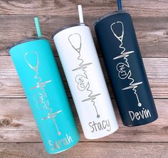 three personalized tumblers are lined up on a wooden surface, one is blue and the other is white