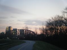 the sun is setting over a bridge and some buildings in the distance with trees on either side