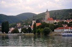 there is a boat on the water in front of some buildings and hills behind it