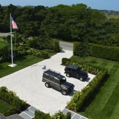 an aerial view of two black suvs parked in a driveway next to a flag pole