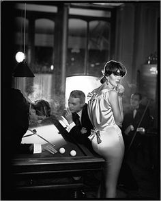 a black and white photo of a woman in a dress standing next to a piano