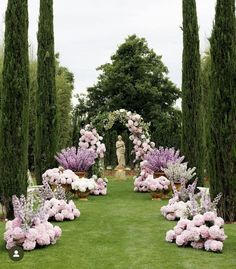 an outdoor garden with pink and white flowers on the ground, surrounded by tall trees