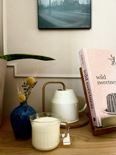 a table topped with a vase filled with flowers next to a candle and a book