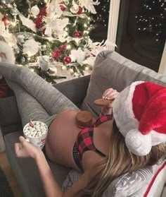 a woman laying on top of a couch next to a christmas tree with popcorn in her hand