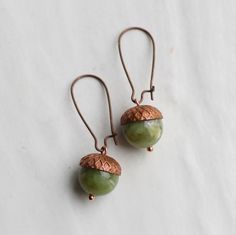 These beautiful green acorn earrings are made from a pearl with an antique copper bead cap.  The tones of the tarnished red copper with the warm olive green of the gemstone look great together.  I have added some co-ordinating earwires in antique copper which match the darkened red of the acorn perfectly.   The length of the earring is about 40mm (around an inch and a half) long, with the green acorns designed to hang around one inch below the earlobe.   This piece of handmade jewellery comes packaged in a nice recycled gift box with a handmade tag, all ready to give or keep. We have more acorn earrings and necklaces here: https://www.etsy.com/uk/shop/SilkPurseSowsEar?ref=hdr_shop_menu&search_query=acorn 🖤 FASTER SHIPPING 🖤 Need this fast? We offer a Faster Shipping option here: https:// The Tarnished, Acorn Jewelry, Acorn Earrings, Autumn Earrings, Art Nouveau Earring, Engraved Locket, Silk Purse, Handmade Tags, Fall Earrings