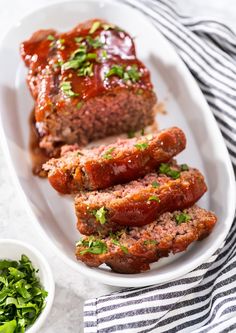 meatloaf on a white plate with sauce and green salad in a bowl next to it