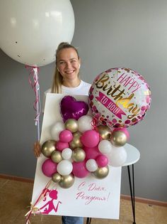 a woman holding balloons and a sign with the words happy birthday written on it,