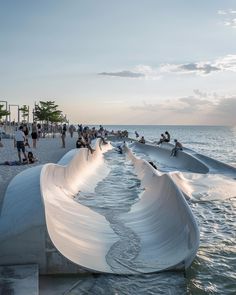 people are standing on the beach next to an artistic sculpture